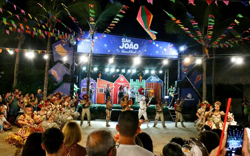 a imagem mostra pessoas curtindo os shows de São João no Beach Park. É possível ver um palco com bandas, bandeirinhas de festa junina e pessoas assistindo em frente ao palco