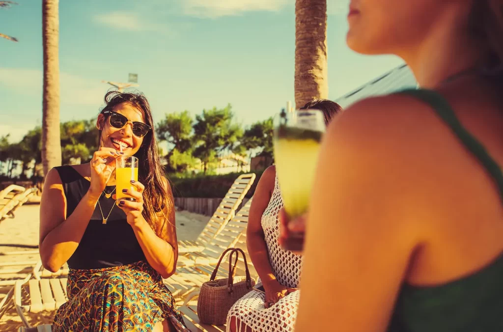 a imagem mostra amigas felizes na hospedagem do Beach Park, aproveitando momentos de drinks e pé na areia em frente ao mar da Praia do Porto das Dunas, Ceará