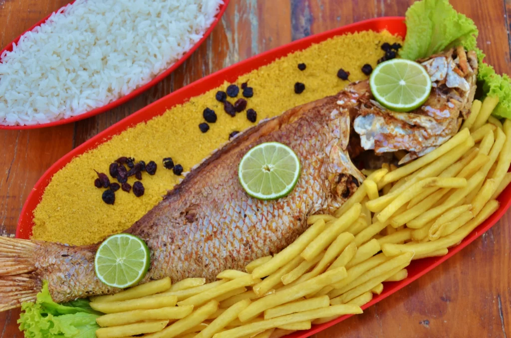 a imgem mostra um peixe assado com batata-frita, farofa e limões com arroz em uma travessa no restaurante da praia do Beach Park